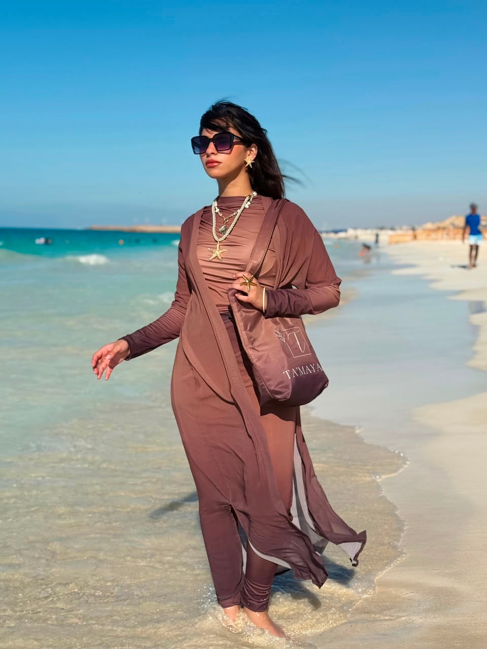 Ta’mayaa modest swimwear brown cover-up with long sleeves and matching bag on beach shore
