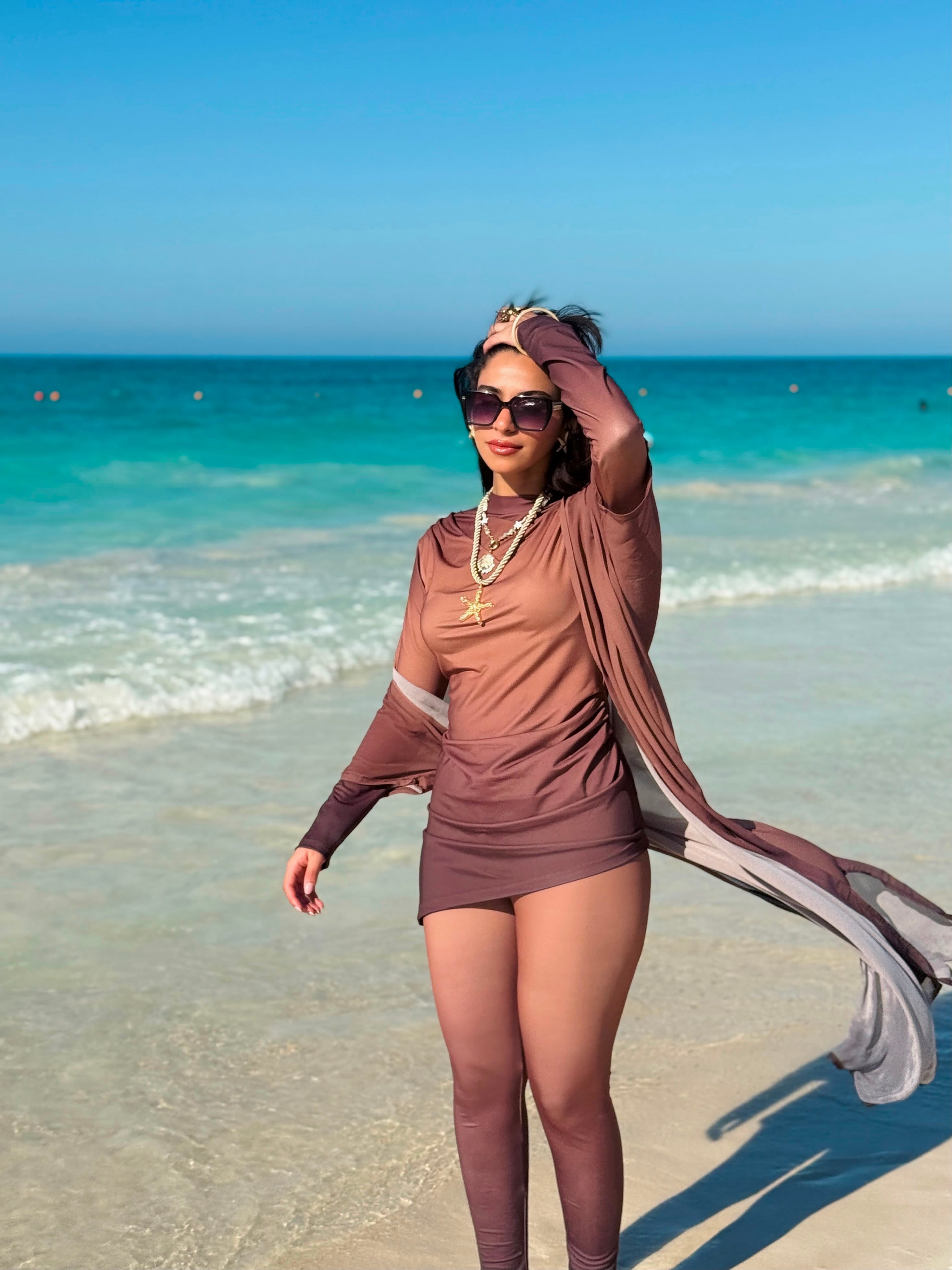 Ta’mayaa swimwear modest brown long-sleeve beach outfit with flowing fabric and sunglasses