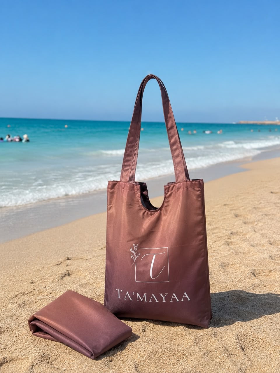 Ta’mayaa brown tote bag and matching swimwear modest fabric on sandy beach near ocean