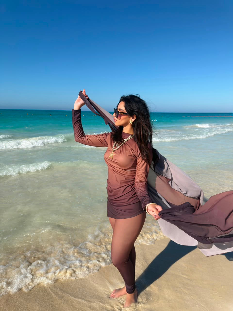 Woman wearing Ta’mayaa swimwear modest set in brown standing on the beach with ocean background
