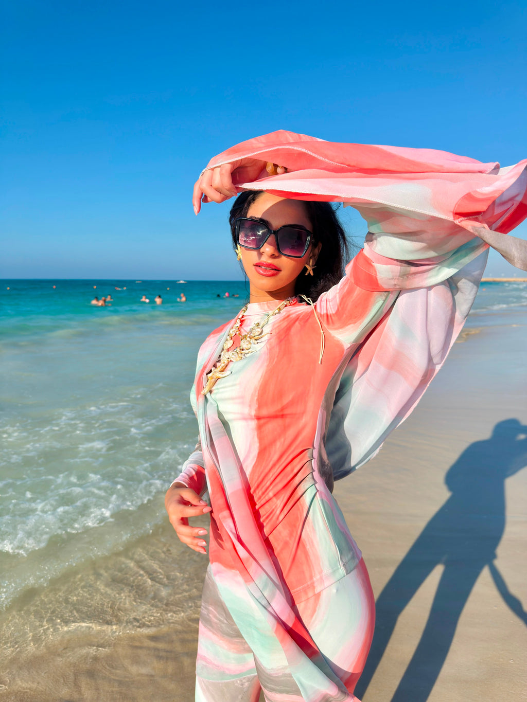 Woman wearing colorful swimmers swimwear by Ta’mayaa posing on a sunny beach with ocean background