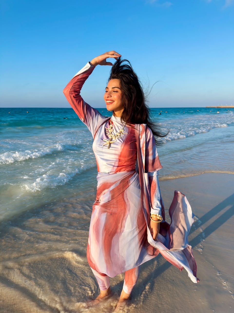 Woman wearing colorful swimmers swimwear by Ta’mayaa standing on the beach with ocean waves in the background