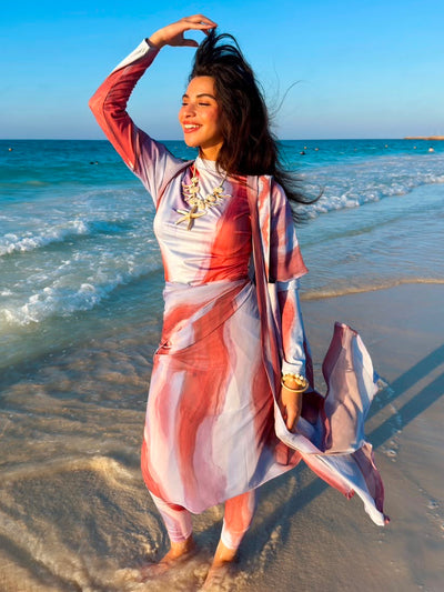 Woman wearing colorful swimmers swimwear by Ta’mayaa standing on the beach with ocean waves in the background