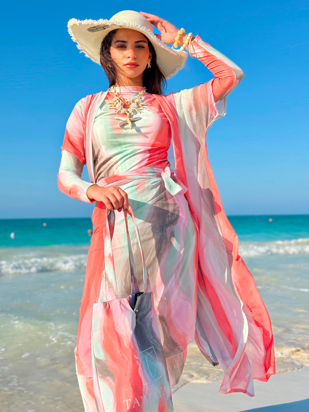 Woman wearing colorful swim cover-up with hat and carry bag by the beach showcasing swimmers swimwear