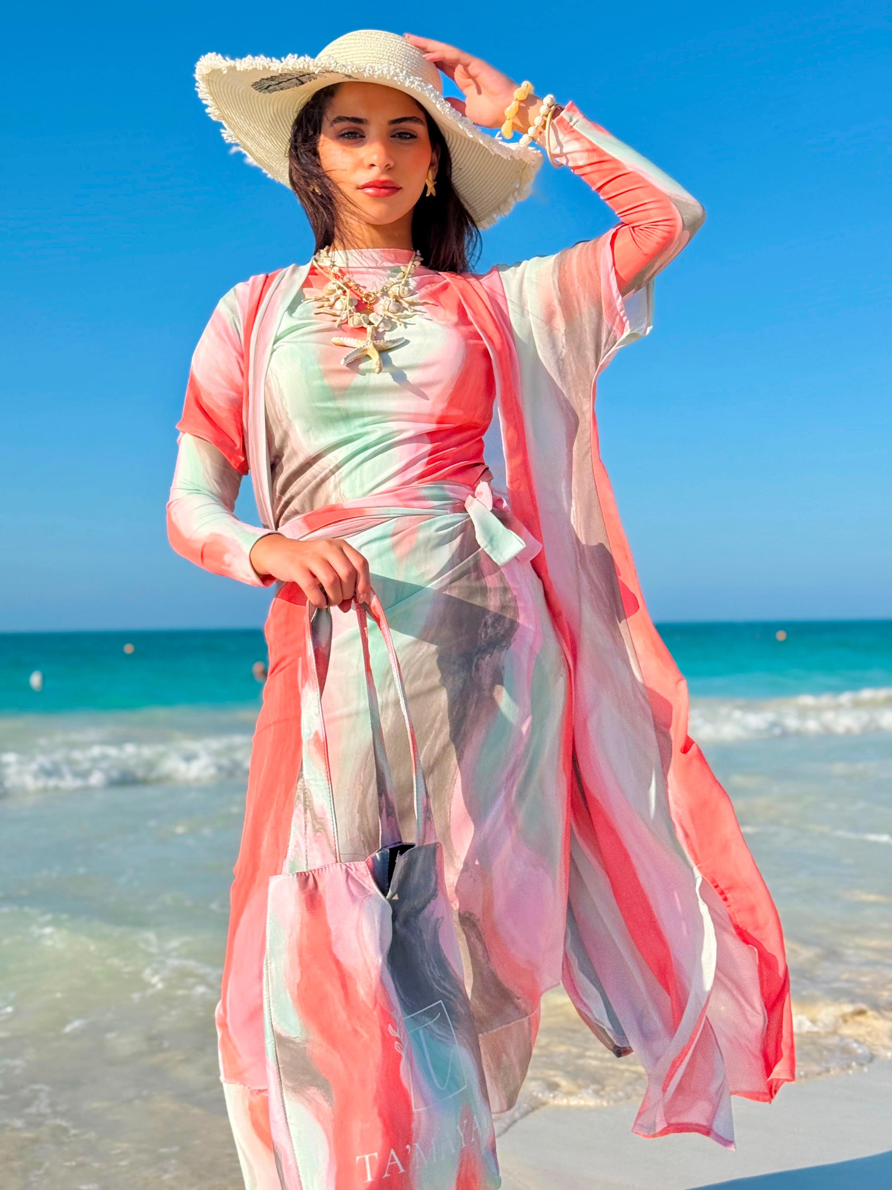 Woman wearing colorful swim cover-up with hat and carry bag by the beach showcasing swimmers swimwear