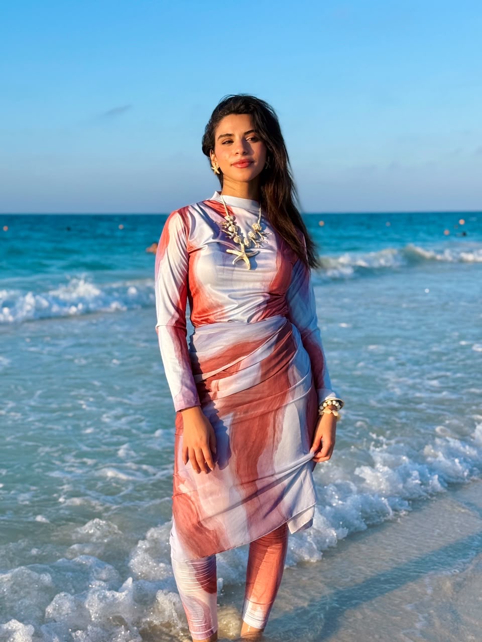 Woman wearing Ta’mayaa swimmers swimwear with long sleeves and matching leggings standing on the beach by the ocean