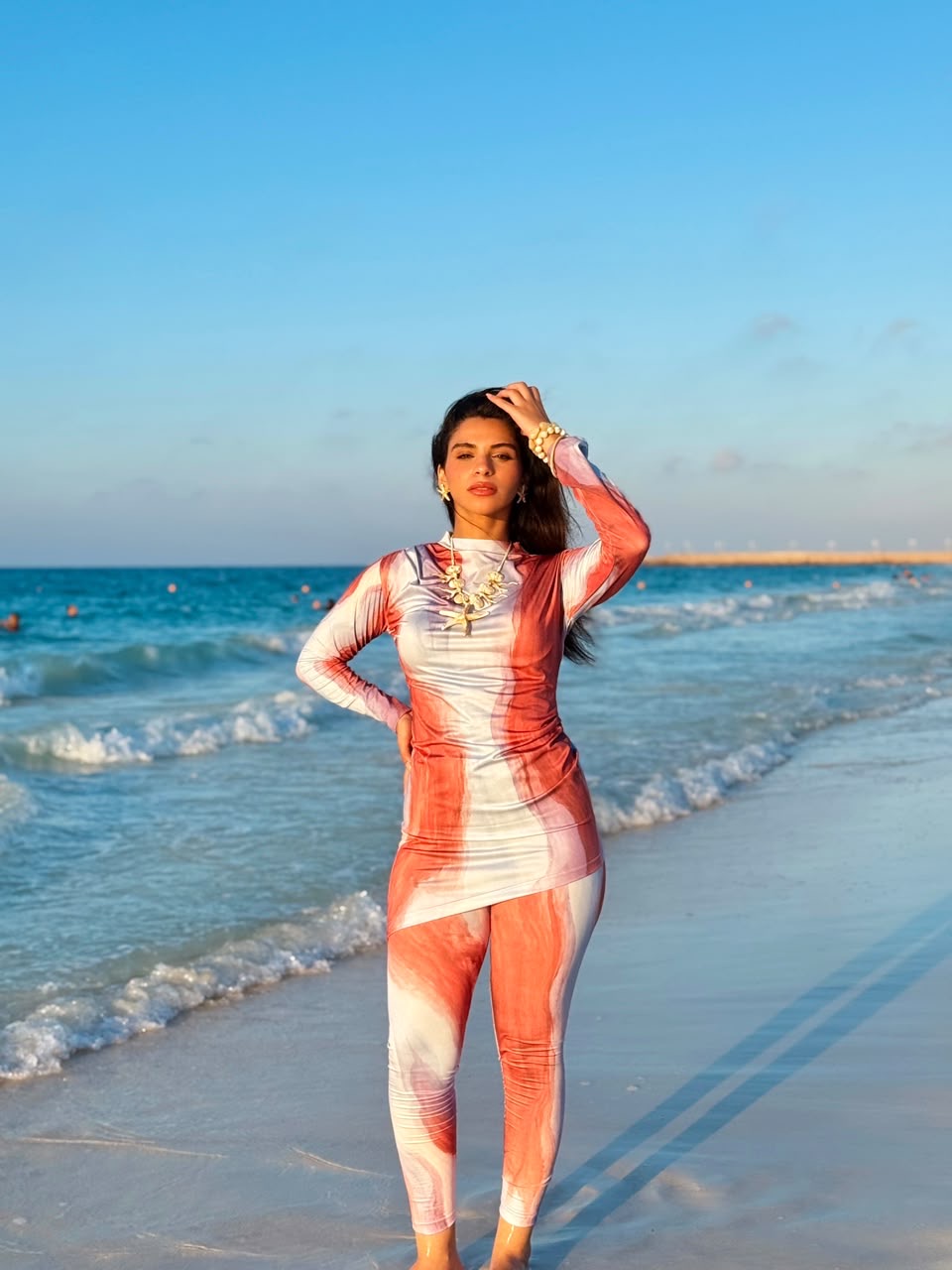 Woman wearing red and white patterned swimmers swimwear standing on beach with ocean waves