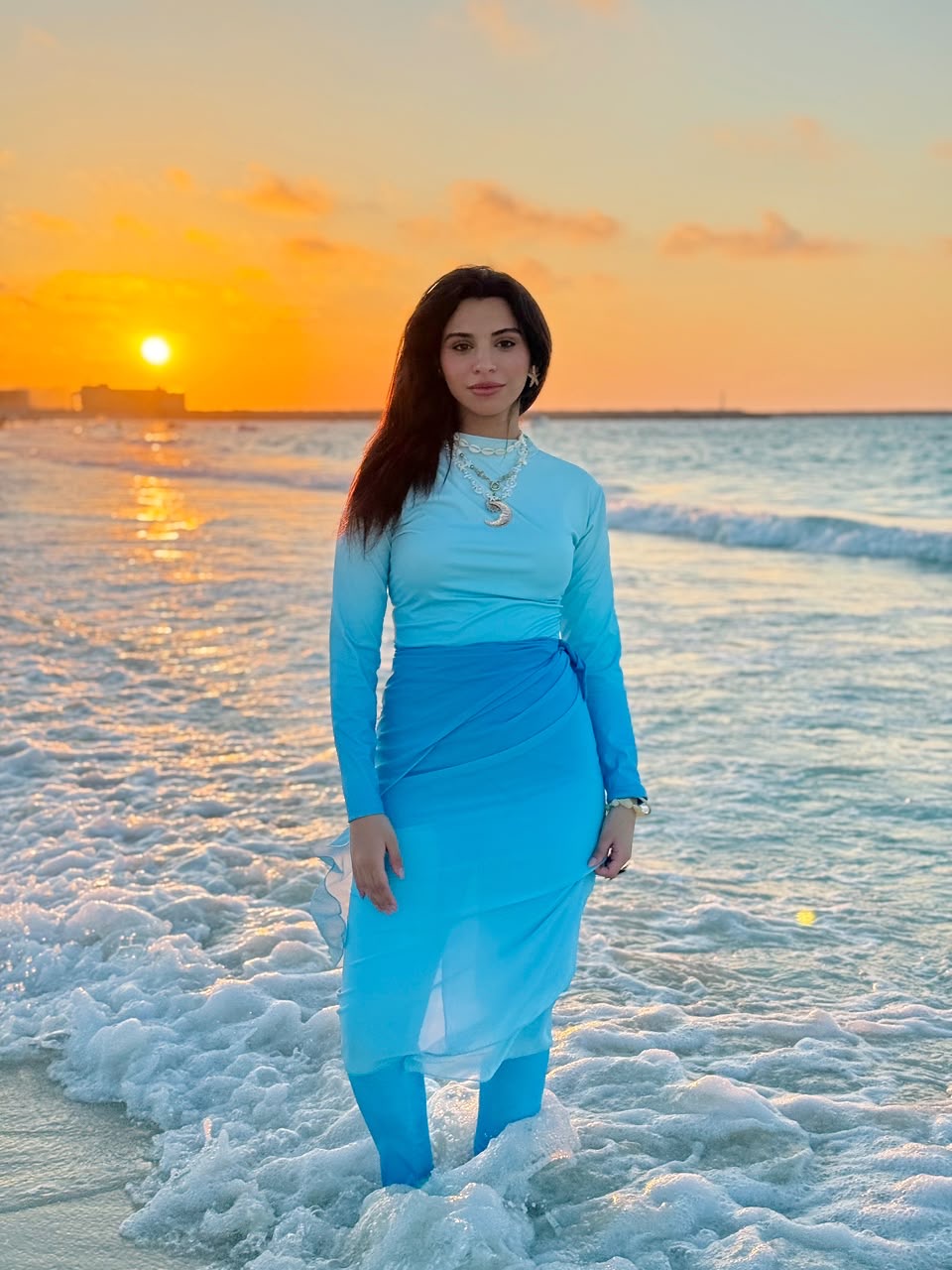 Ta’mayaa swimwear modest blue long-sleeve full coverage outfit worn by woman at beach sunset