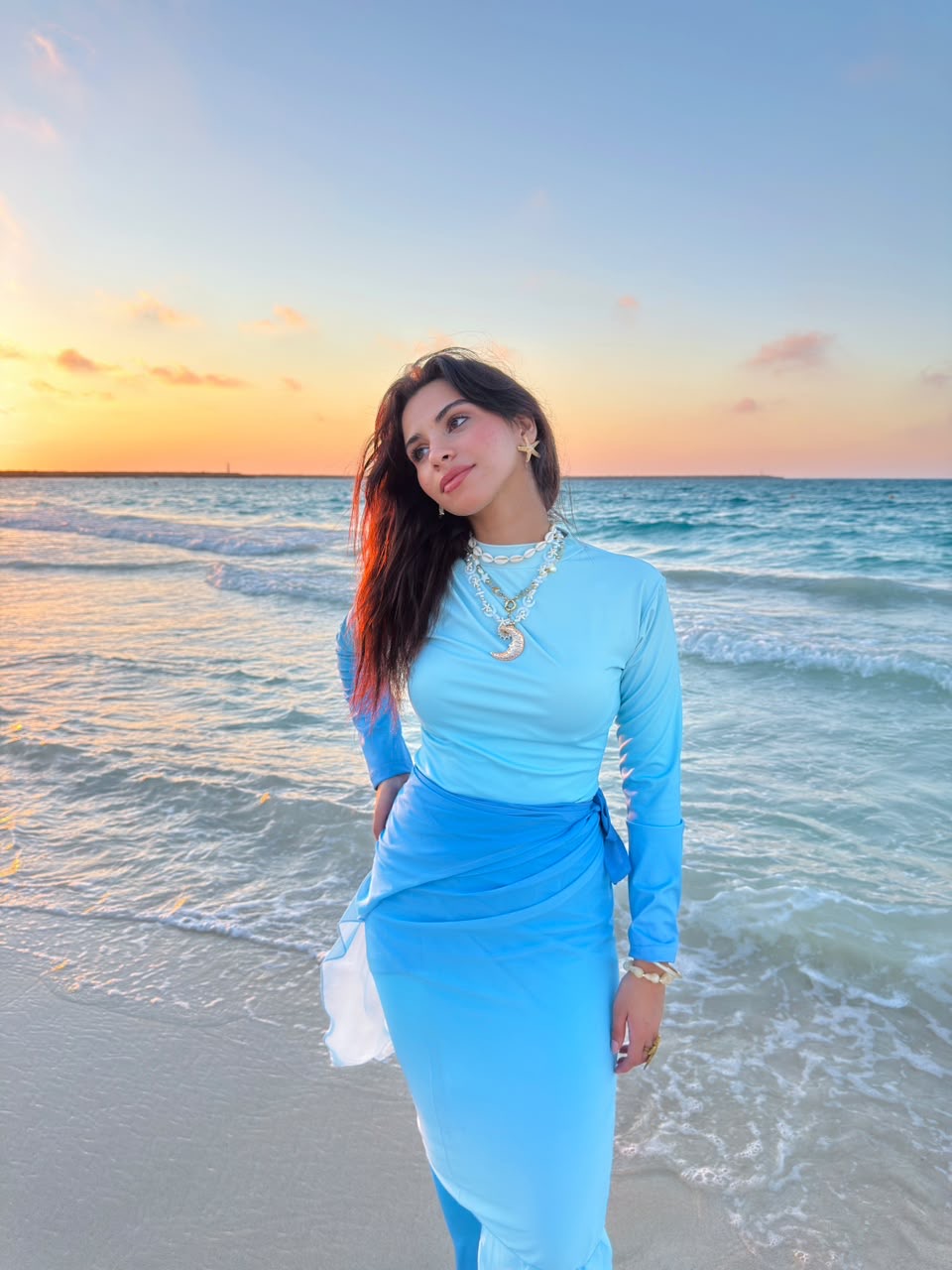 Woman wearing blue swimwear modest standing on the beach at sunset with ocean waves in the background